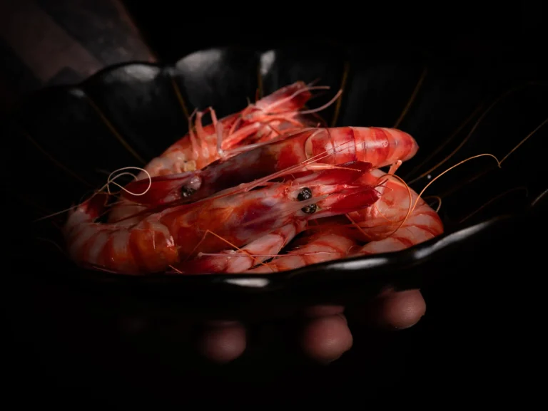 Gambas rojas sostenidas entre unas manos sobre fondo oscuro