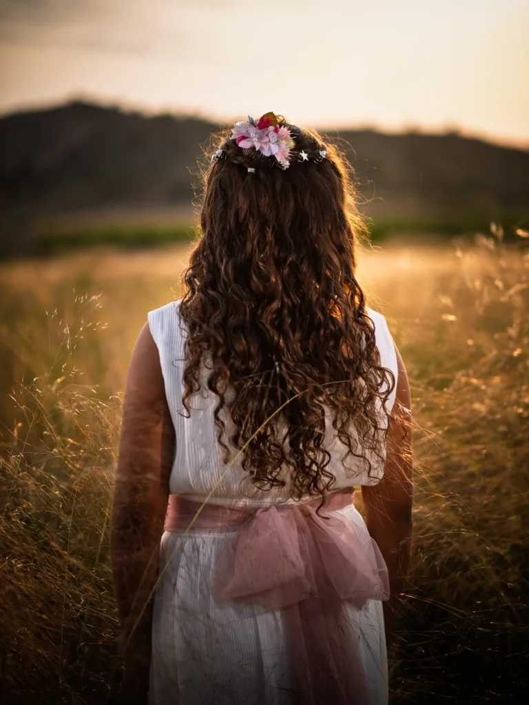 Niña de comunión de espaldas en un campo al atardecer