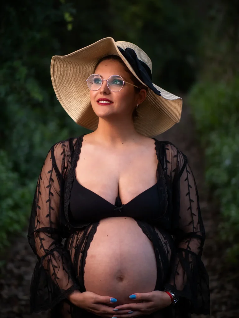 Mujer embarazada con sombrero y vestido negro en el bosque