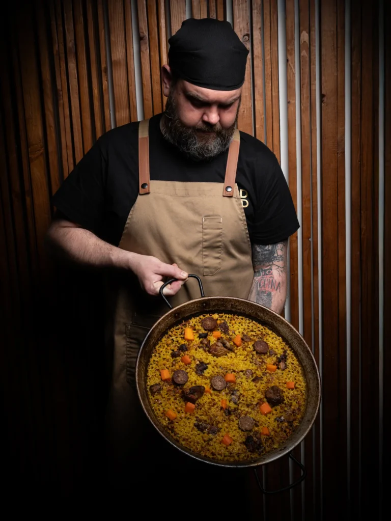 Cocinero sosteniendo una paellera sobre fondo oscuro