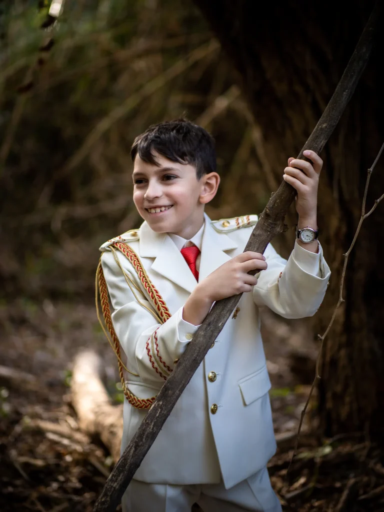 Niño vestido de comunión sosteniendo una rama en el bosque