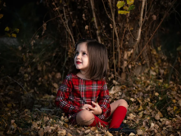 Niña con vestido rojo sentada entre hojas de otoño