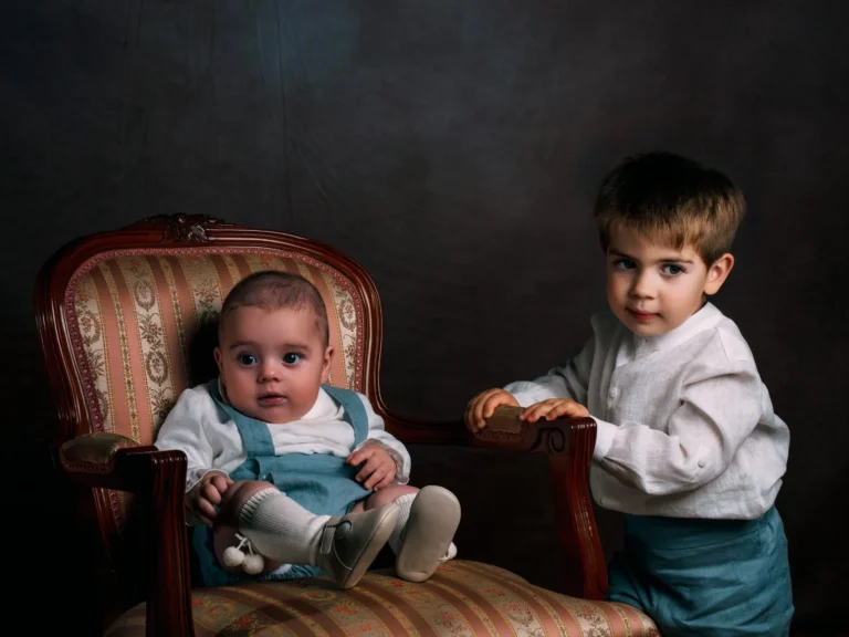 Retrato infantil de dos niños junto a un sillón clásico en estudio