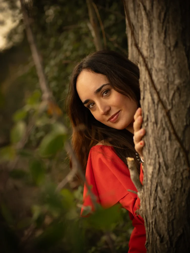 Mujer con vestido rojo asomada tras un árbol