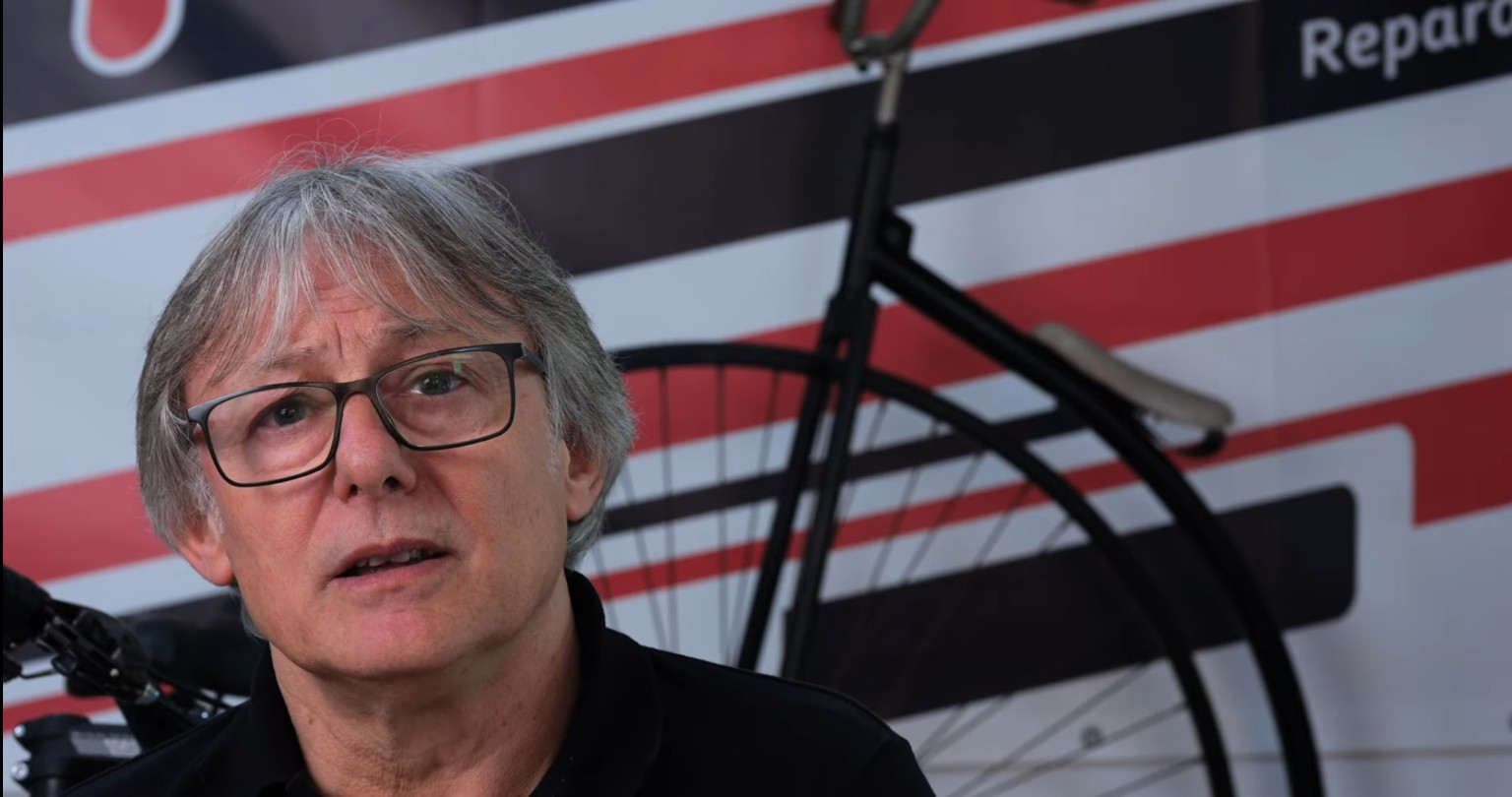 Hombre con gafas entrevistado junto a una bicicleta en Riba-roja, comerç i memòria